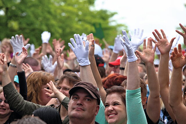 Fotografie einer Menschenmenge die ihre Hände Richtung Himmel strecken und lachen
