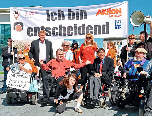 Menschen mit und ohne Behinderungen mit bunten Schildern bei einer Demonstration