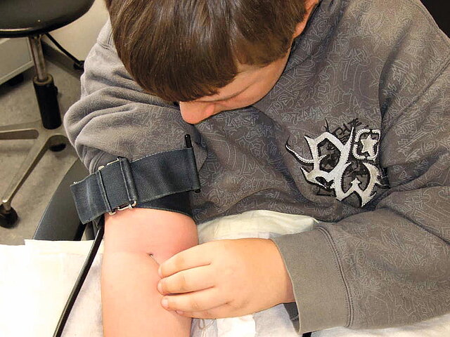 Foto eines Jungen mit Stauband am Arm, der sich eine Nadel in die Armbeuge sticht.