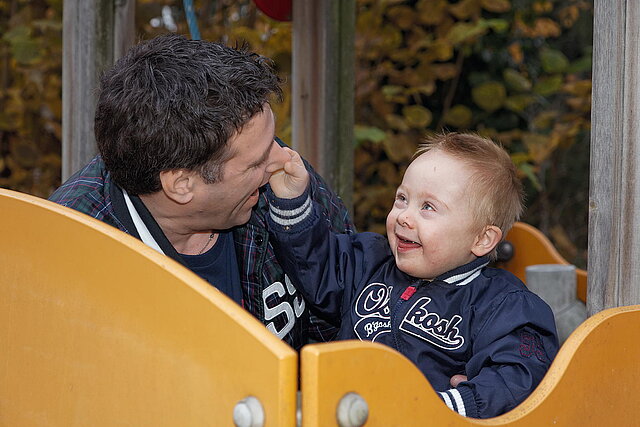Foto eines lachenden behinderten Kindes mit seinem Vater