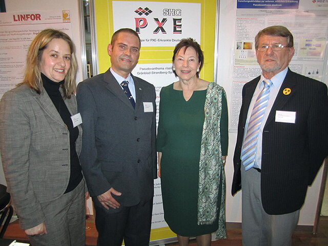 Vier Personen blicken vor einem Banner der Selbsthilfegruppe für PXE-Erkrankte Deutschlands e. V. lächelnd in die Kamera